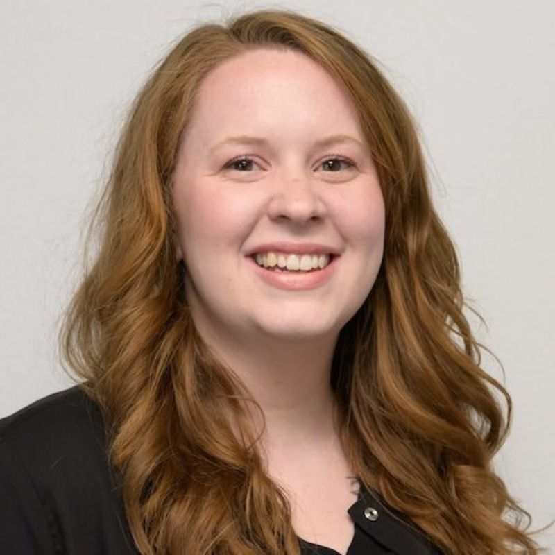 Dr. Bethany Staten, audiologist, smiling with long auburn hair in a black top